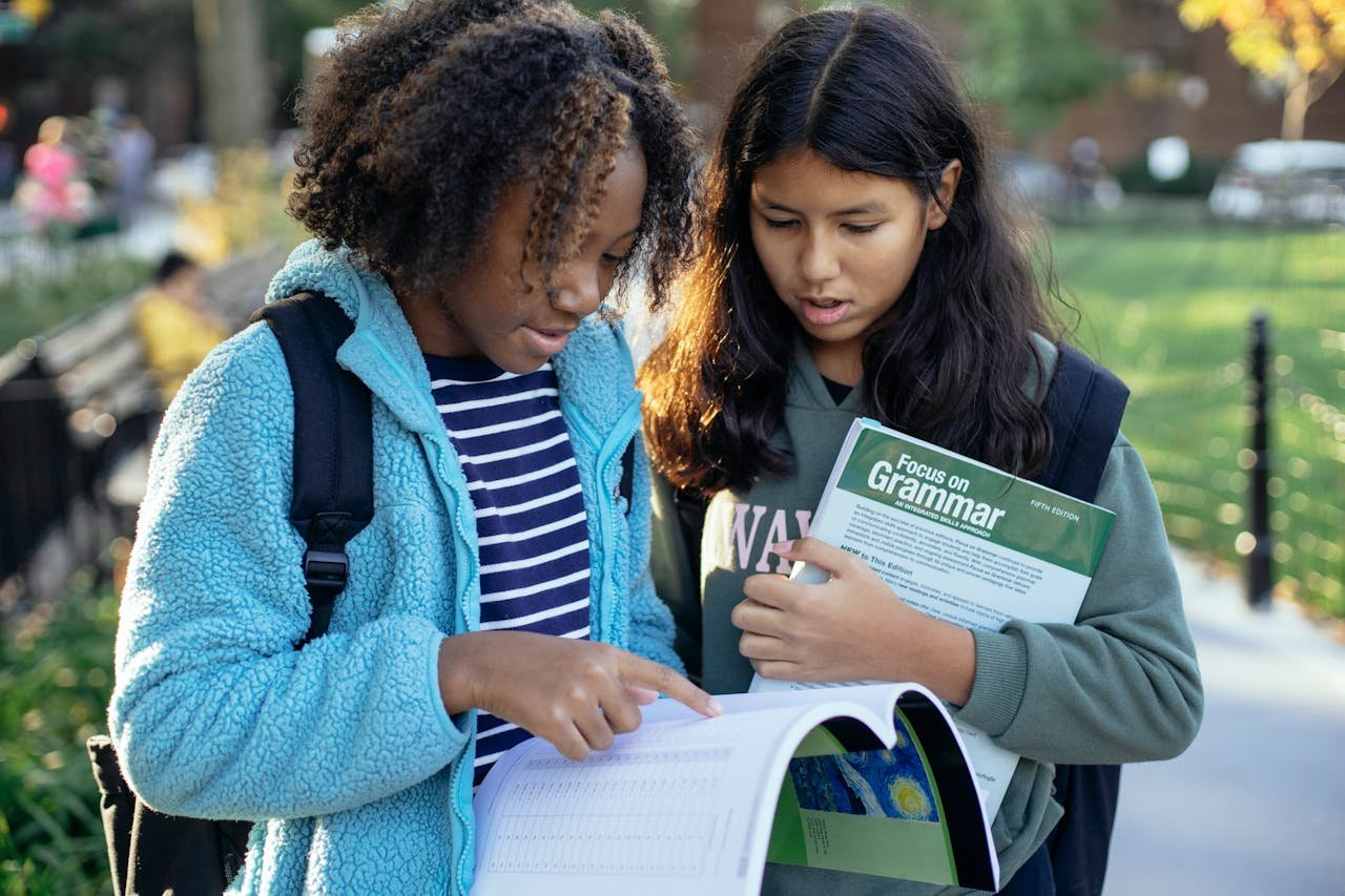 contact-img Focused diverse classmates with backpacks holding textbooks and studying while spending time in park